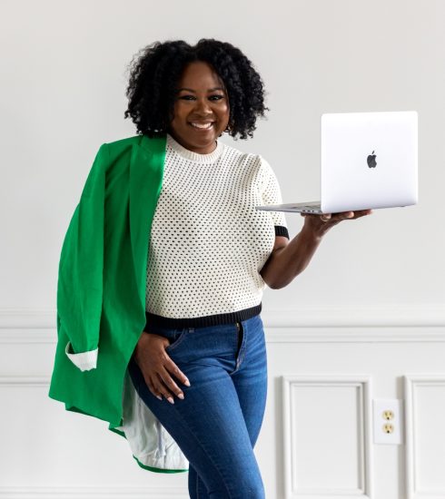 Tomiko Harvey SEO Coach holding a white Apple MacBook Air up with her left hand.