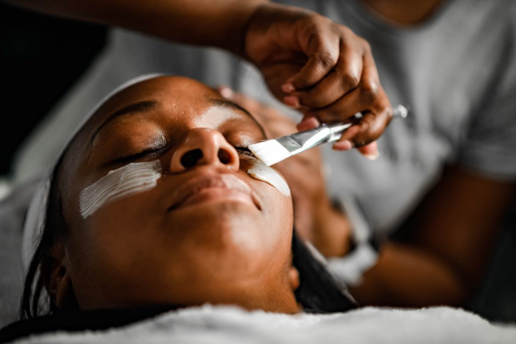 Image depicts Black woman getting a relaxing skincare treatment with esthetician.