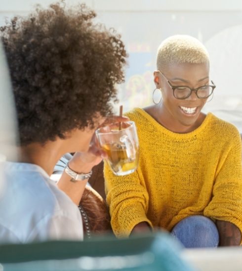 two black women living boldly over 40. Having a drink and conversation in a casual setting.