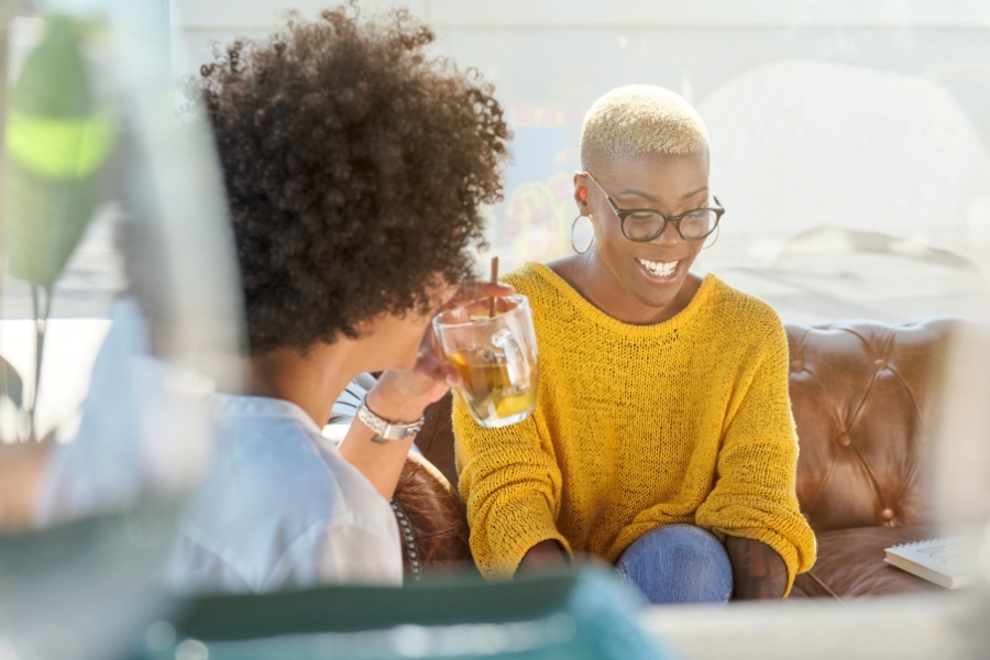 two black women living boldly over 40. Having a drink and conversation in a casual setting.