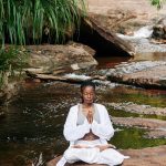 Black women meditating, sitting on a rock by a quiet tropical stream for personal growth