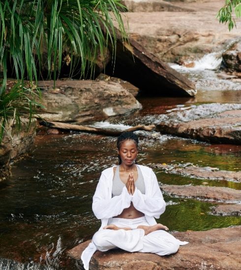 Black women meditating, sitting on a rock by a quiet tropical stream for personal growth