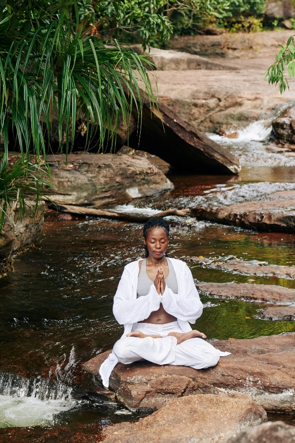 Black women meditating, sitting on a rock by a quiet tropical stream for personal growth