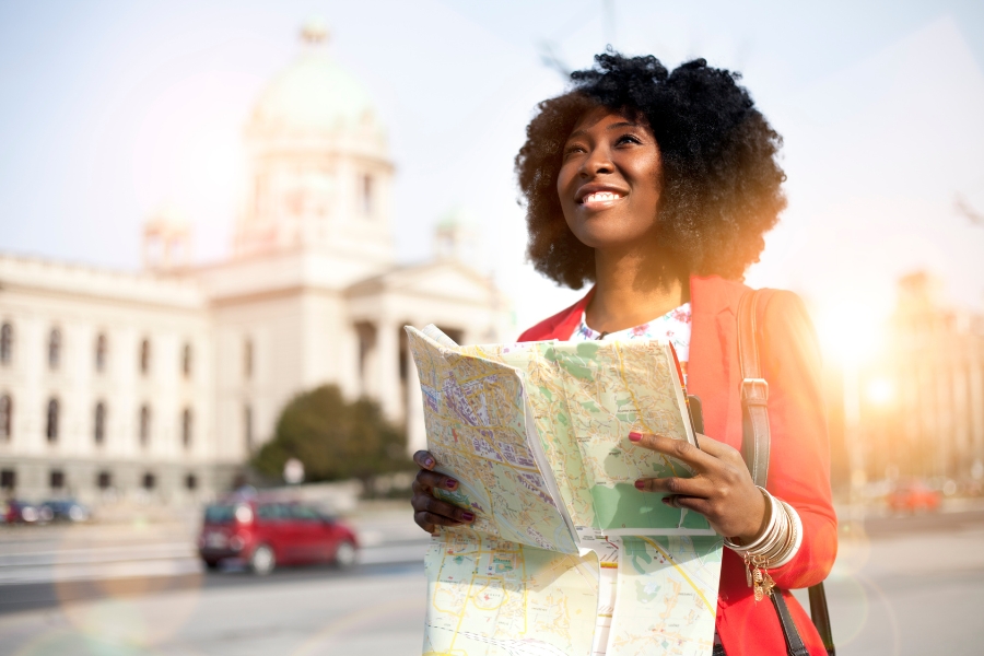 Black woman solo traveling smiling and holding a map